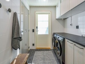 A compact laundry room with a washing machine, a bench, and a door leading to a bright area.