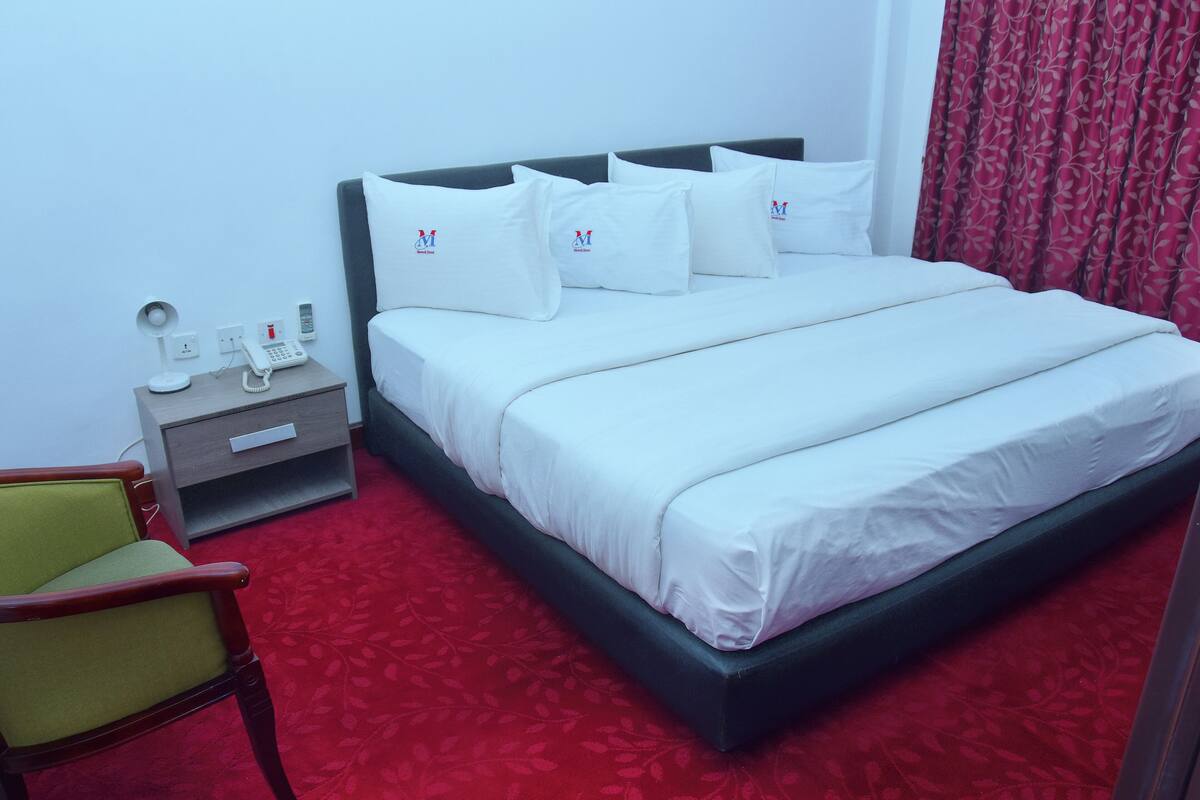 A hotel room with a bed, a nightstand, a chair, and a telephone.