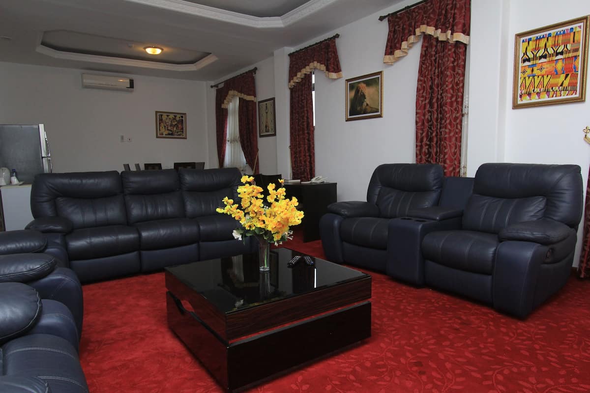 A living room with a black leather sofa set, a glass coffee table with a vase of yellow flowers, and red patterned carpet.