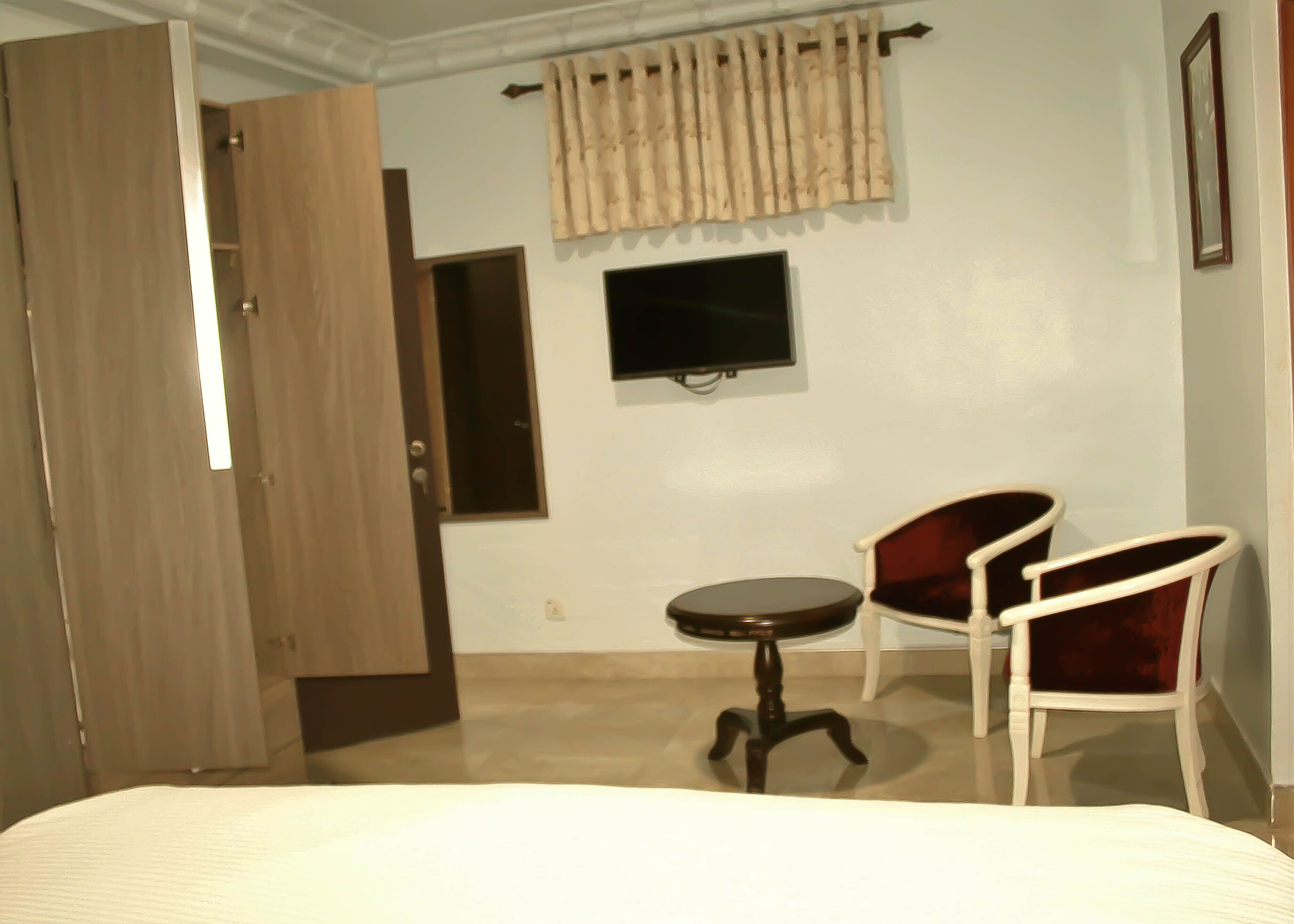 A hotel room with a bed, a desk, a chair, a television, and a wardrobe.