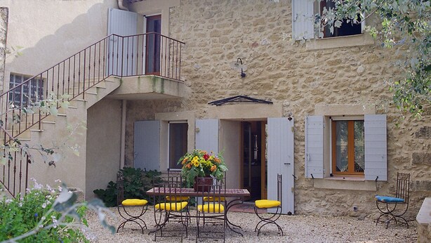 A stone building with a balcony, a table with chairs, and a flower arrangement. - Typical Provencal farmhouse (Villelaure)
