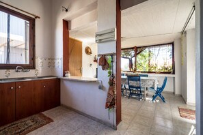 Une cuisine avec des meubles de rangement en bois, un évier et une fenêtre. On y trouve également un coin repas avec des chaises bleues et une table.