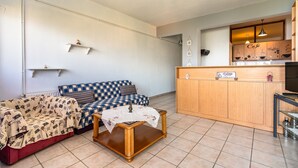 Un espace de vie chaleureux comprenant un canapé, une petite table et un coin cuisine avec des meubles en bois et un espace dédié à la préparation du café.