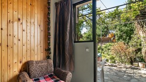 Ein Zimmer mit einer Holzwand, einem gemusterten Sofa, einer Karo-Decke und Blick auf einen Garten durch eine Glastür.
