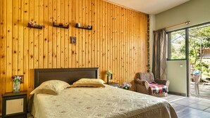 Ein Schlafzimmer mit Holzwand, einem Bett mit Quilzudecke, einem Nachttisch, einem Sessel und Blick durch eine Glastür.
