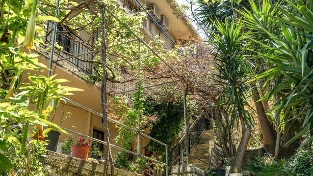 Ein schmaler Gang mit einer Steinmauer, Pflanzgefäßen und einem Gebäude mit einem Balkon.
