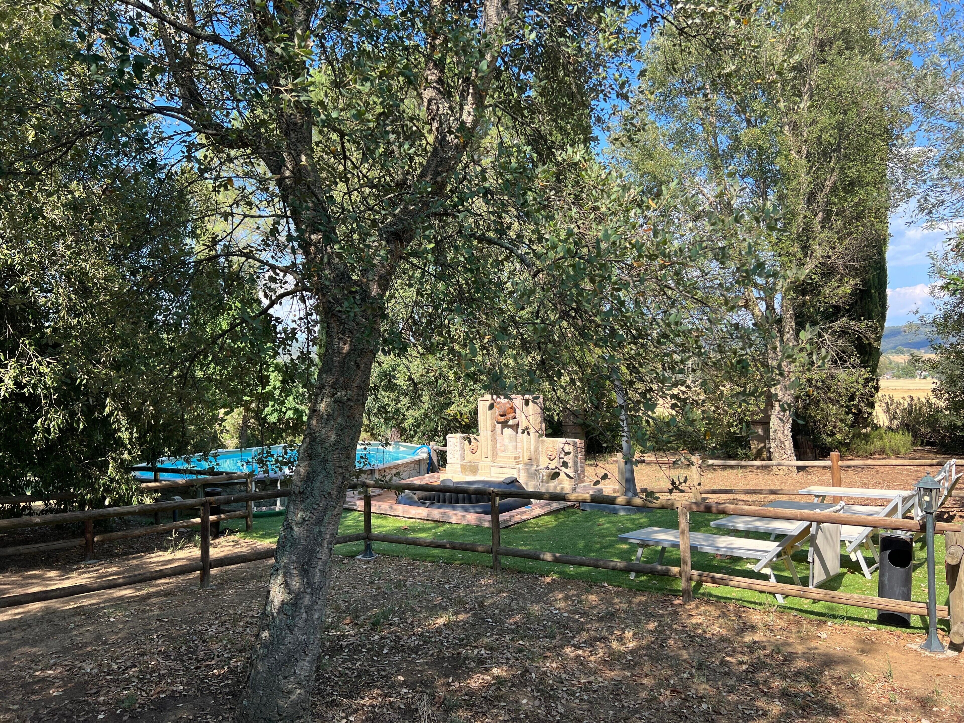 Zona exterior tancada amb taules de picnic, una construcció de pedra i una piscina al fons.