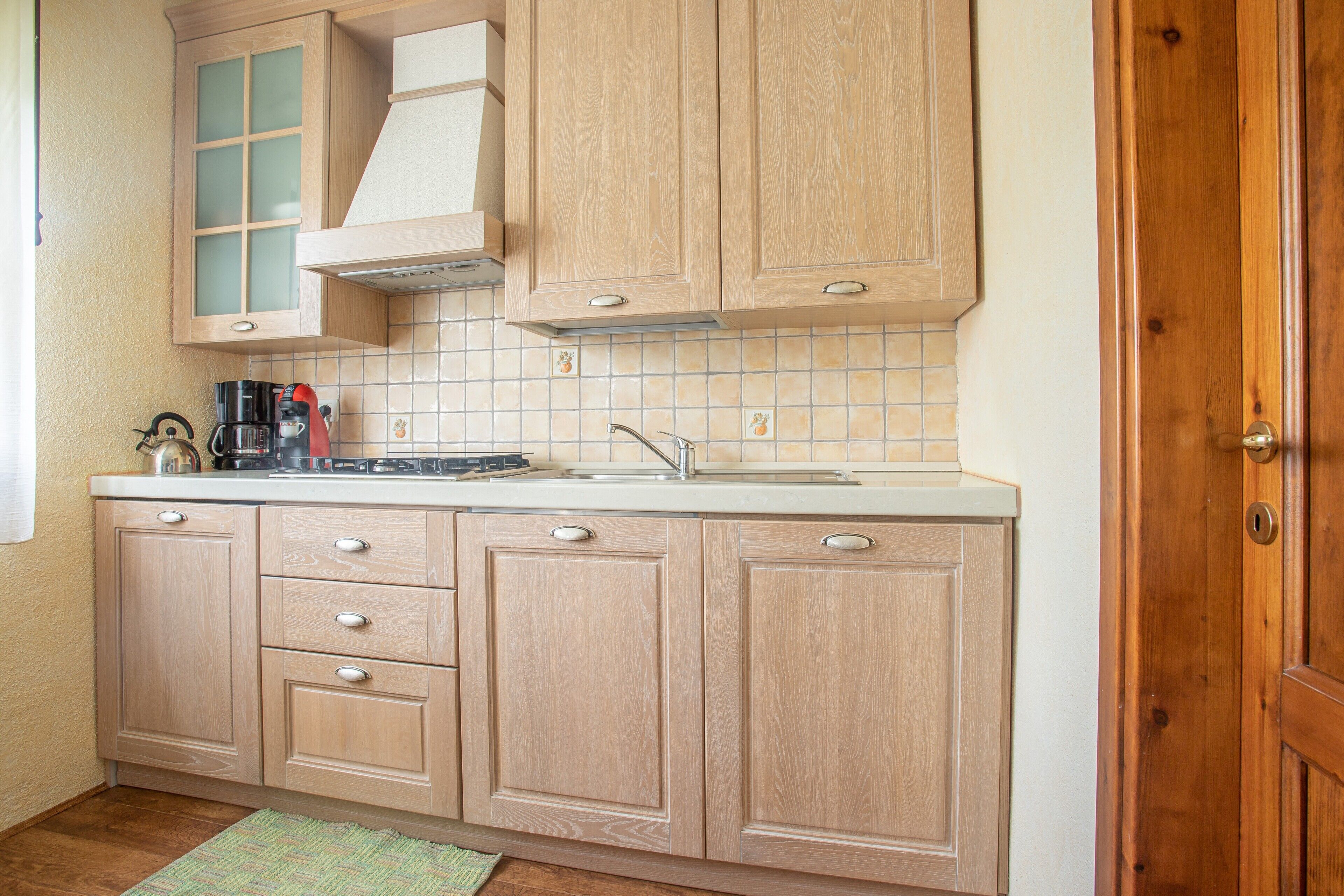 A kitchen with wooden cabinets, a tiled backsplash, a coffee maker, and a sink.