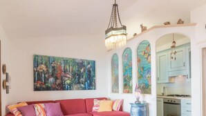 Un salon avec un canapé rouge, un grand tableau abstrait et une cuisine visible à travers une arche.