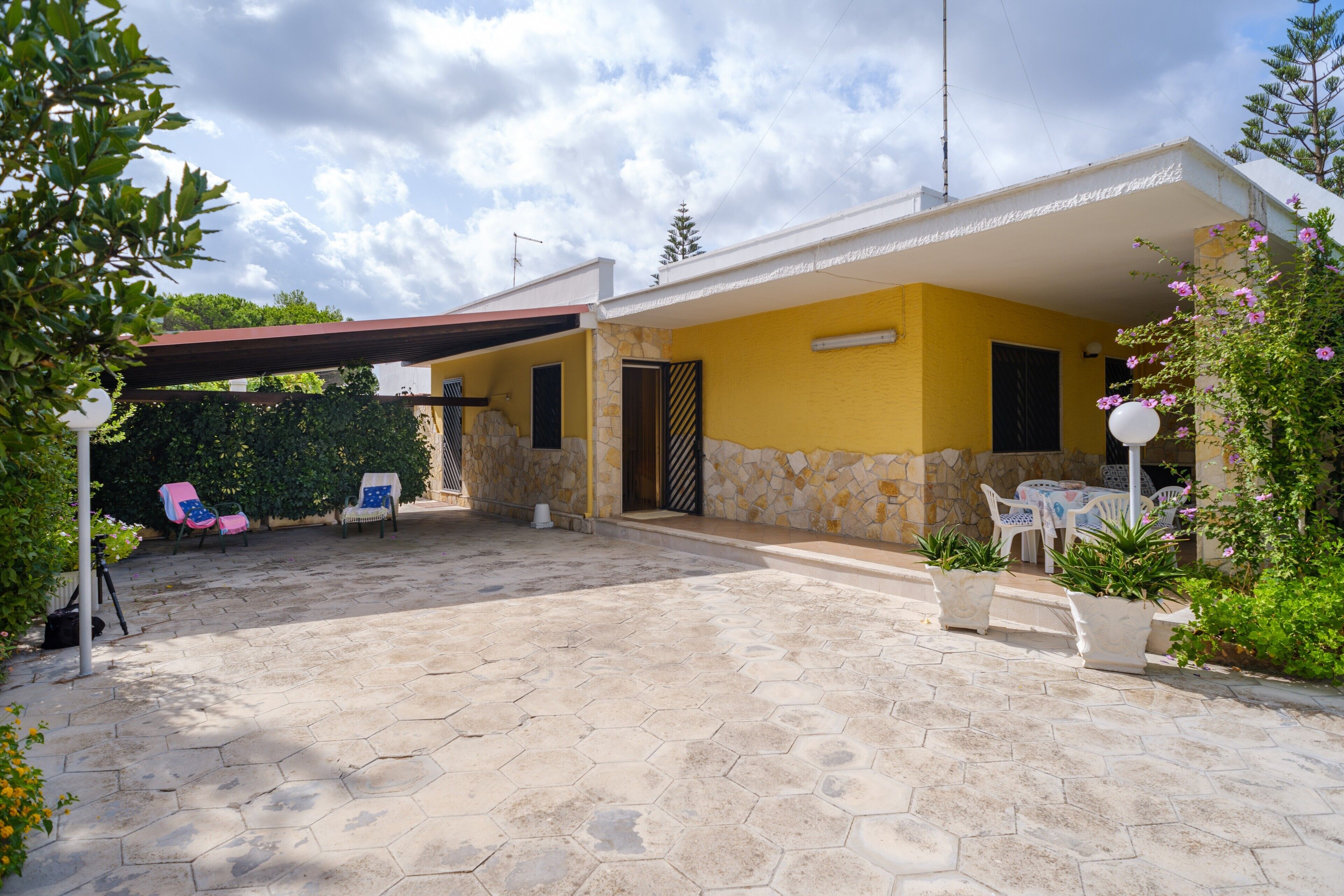 Une maison jaune avec une façade en pierre, un patio couvert et des sièges à l’extérieur.