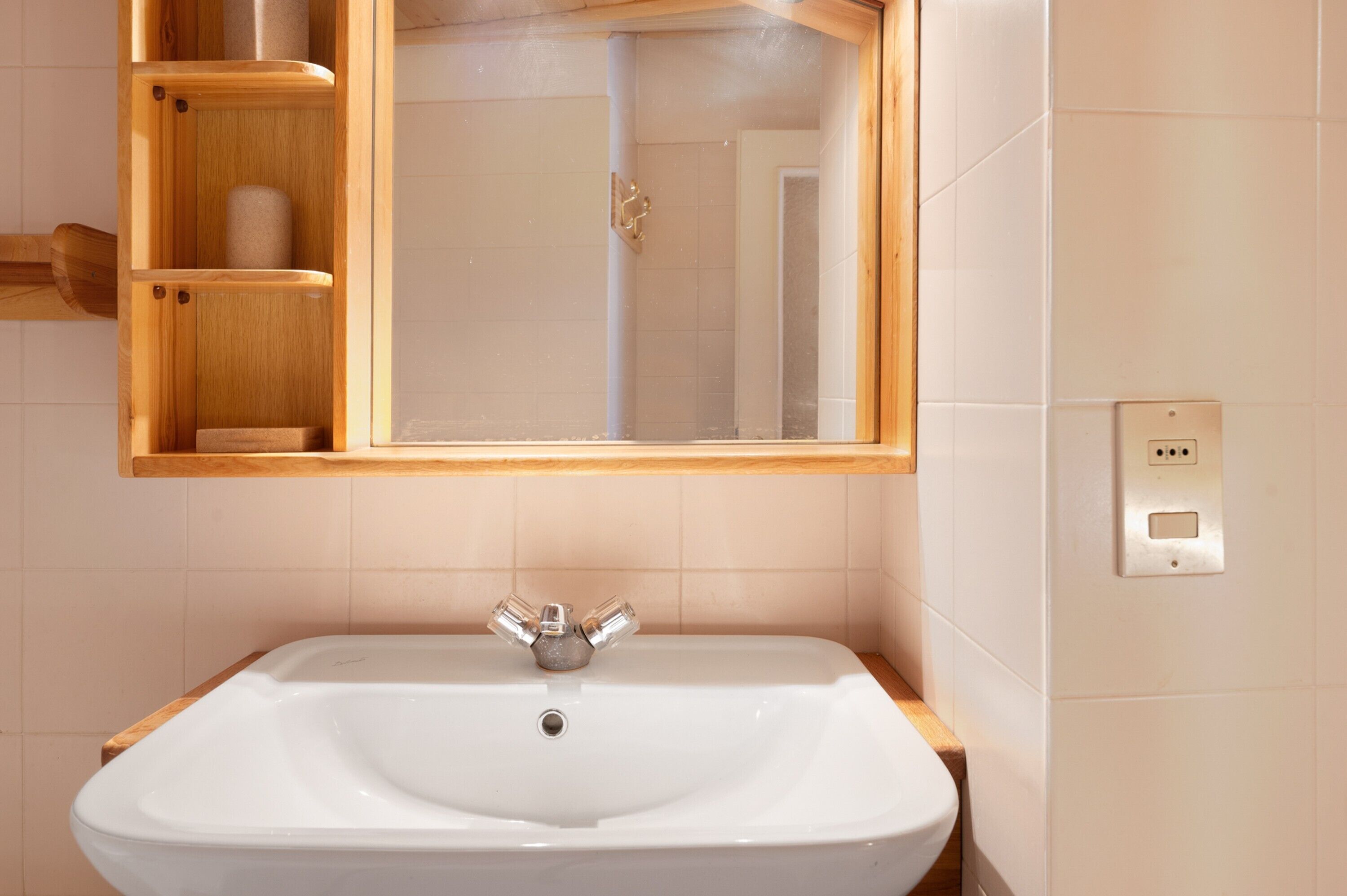 Une salle de bain avec un lavabo blanc, des étagères en bois, un miroir et un distributeur de serviettes.