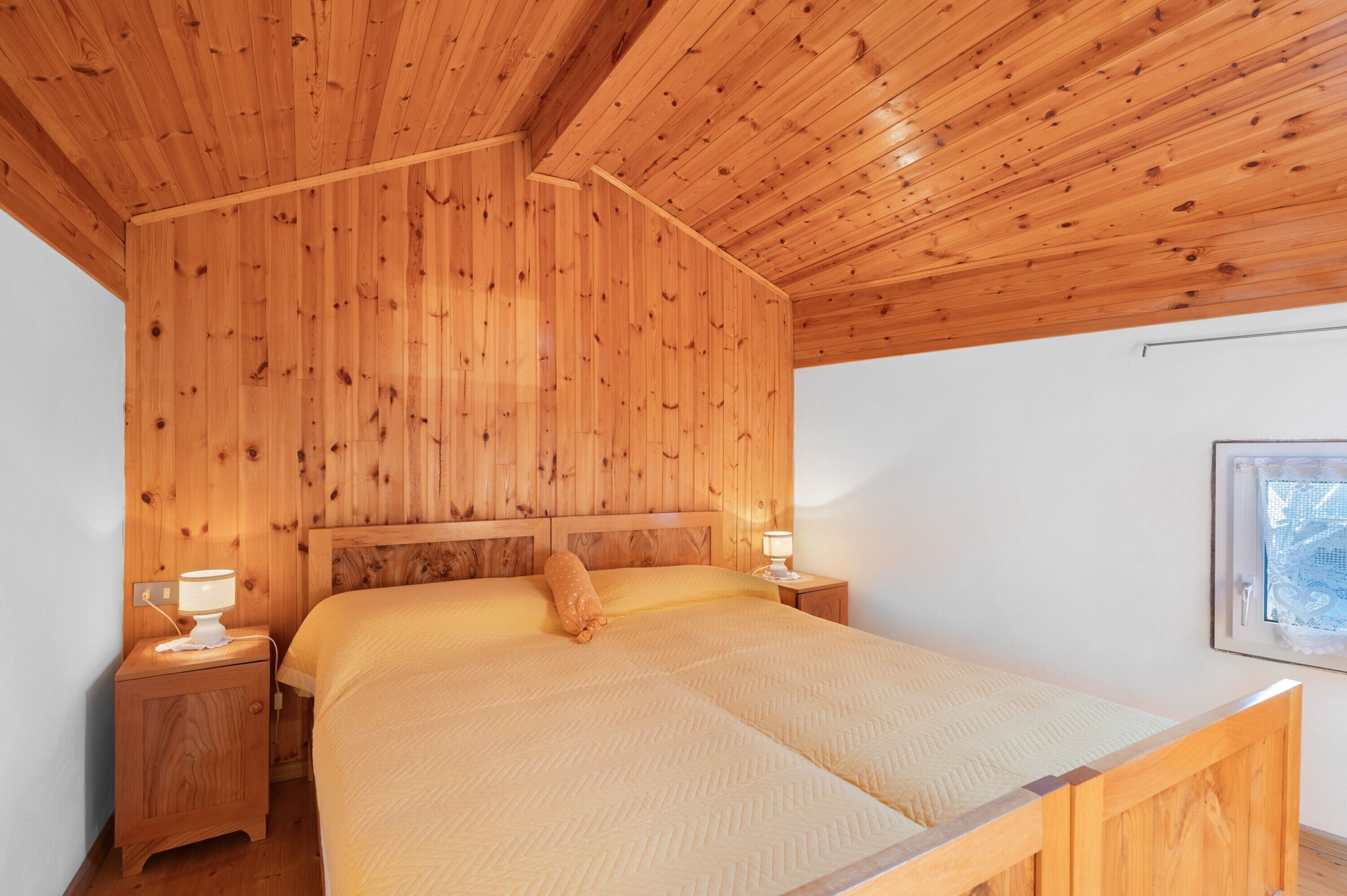 Ein Schlafzimmer mit Holzwänden, einem Bett, Nachttischen und einem Fenster.