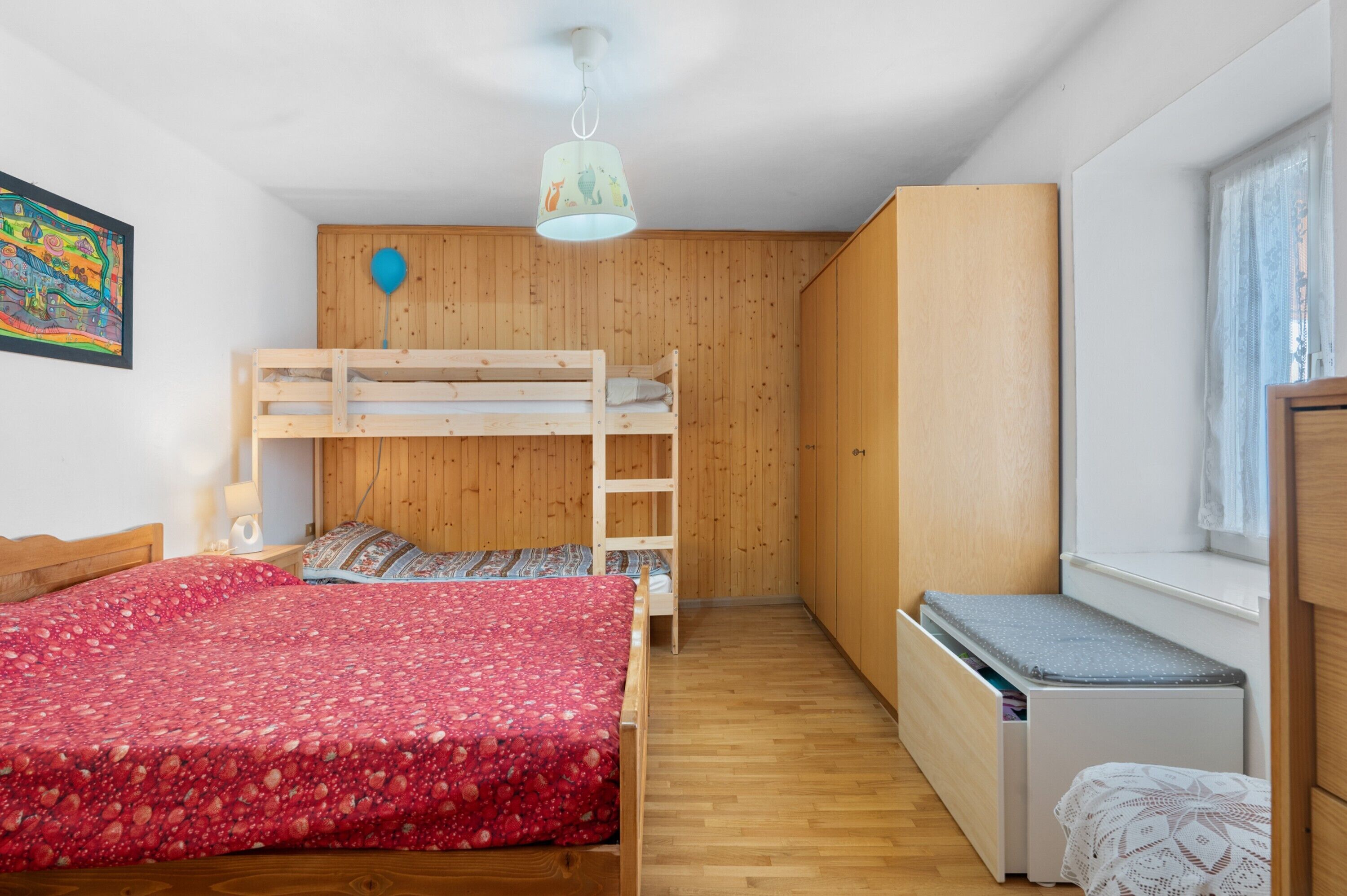 Una camera da letto con un letto a castello, una scrivania, una sedia, una finestra con tende e una lampada a soffitto.