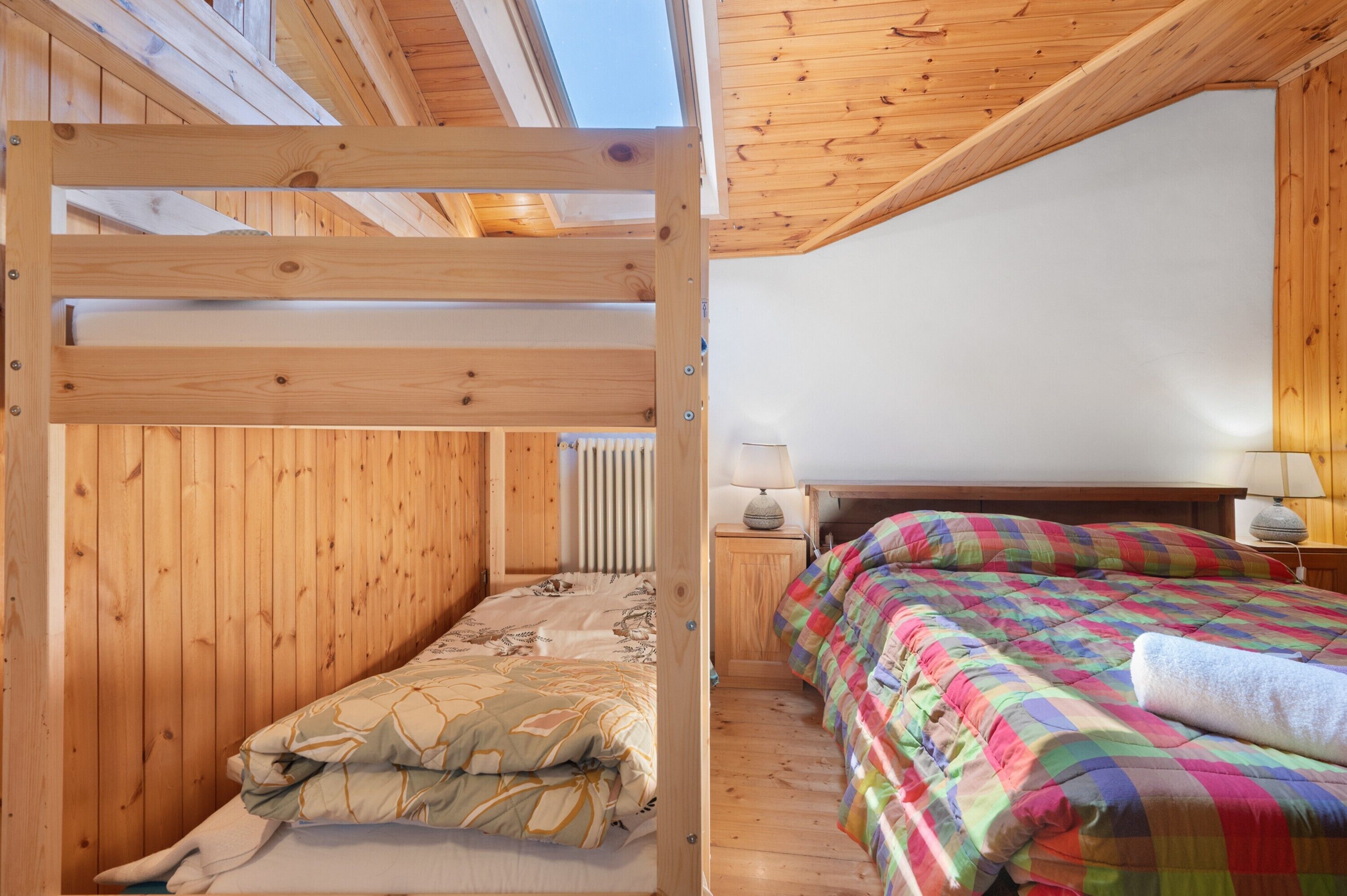 Een houten kamer met stapelbedden, een nachtkastje met een lamp, en een raam.