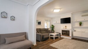Un salon comprenant un canapé, une table basse, une cheminée et un téléviseur fixé au mur.