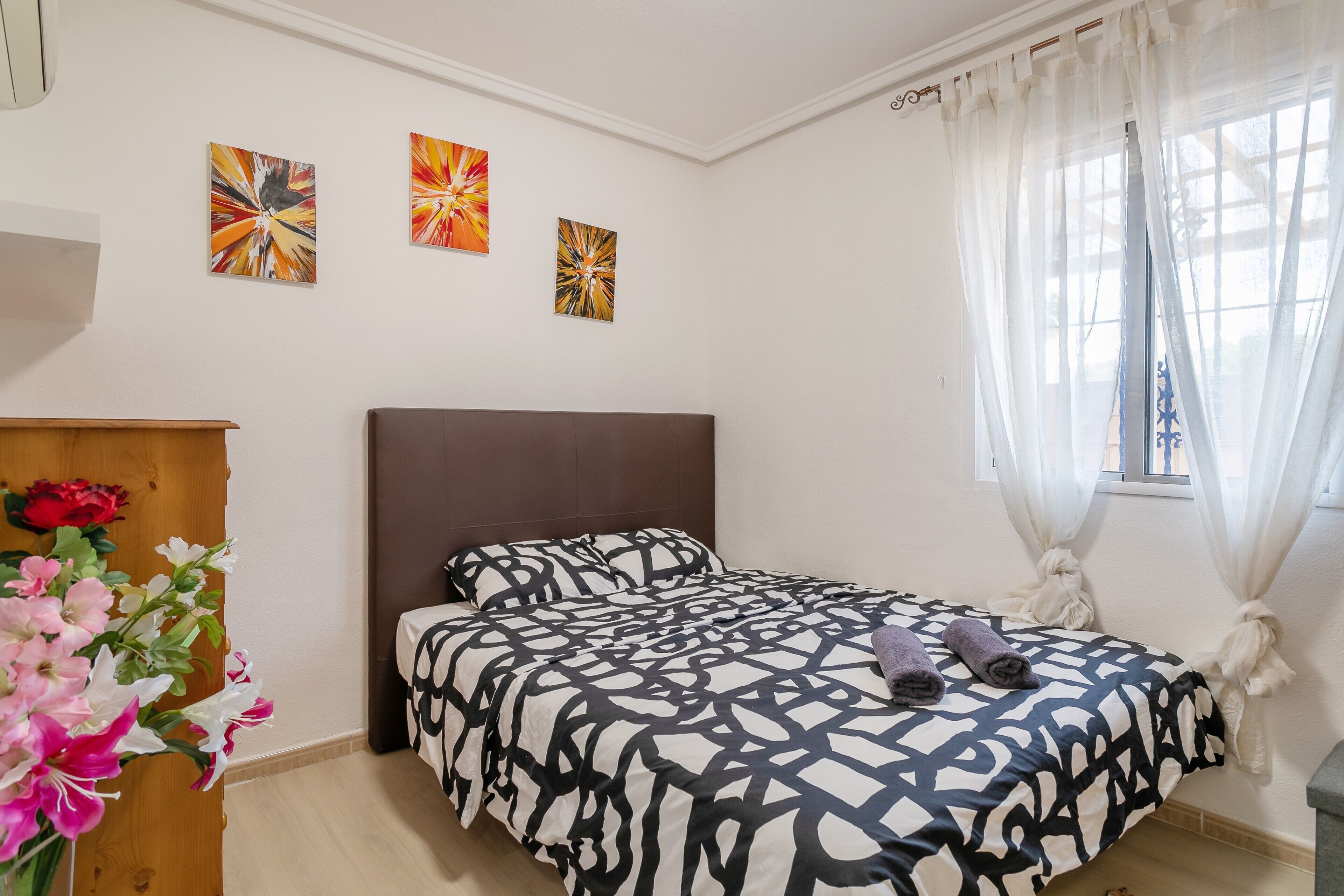 Quarto com cama, cómoda de madeira e janela com cortinas leves.