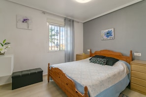 Un dormitorio con una cama, mesitas de noche, una ventana con cortinas, un radiador y una obra de arte colgada en la pared.