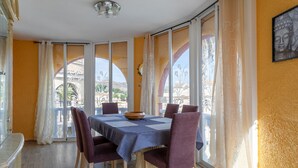 Un coin repas avec une table dressée pour six personnes, de grandes fenêtres avec des rideaux et une statue de Bouddha accrochée au mur.