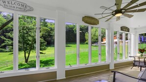 Uma sala de sol com grandes janelas, um ventilador de teto e uma placa que diz 'WELCOME TO OUR PORCH'.