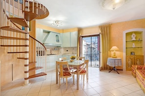 A spacious living area with a dining table, chairs, a sofa, and a spiral staircase.
