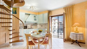 Een moderne keuken met een spiltrap, een eethoek met een tafel en stoelen, en een uitzicht door een groot raam.