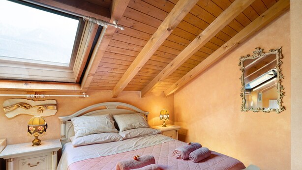 Een slaapkamer met een bed, bedlampen, een nachtkastje, een spiegel en een raam.