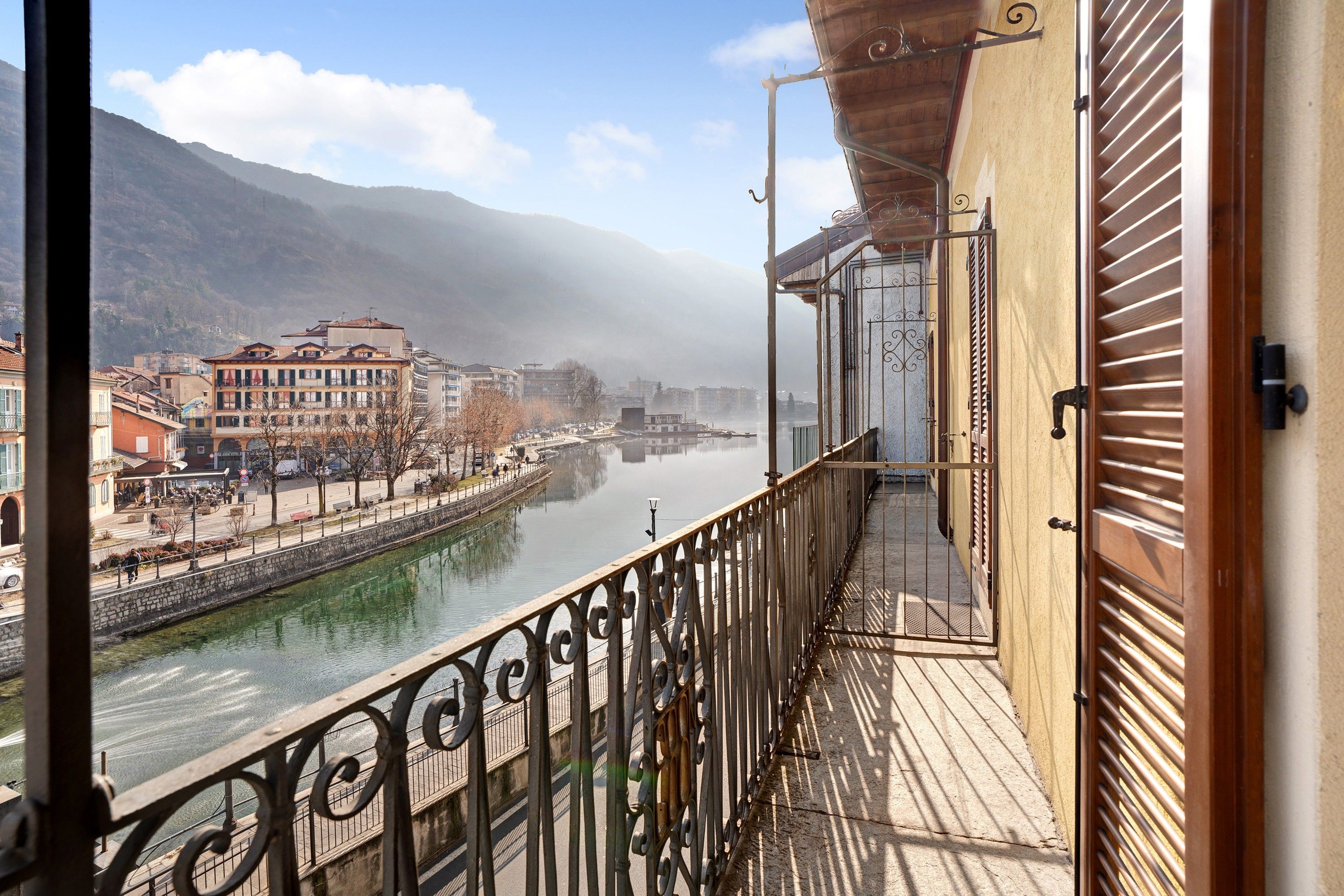 Ein Balkon mit Blick auf einen Fluss und Gebäude, einem Metallgeländer und einer Tür mit Griff.