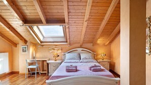 Een slaapkamer met schuine wanden, een dakraam, een bed met hoofdeinde, nachtkastjes met lampen, een bureau en een stoel.