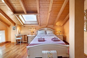 Une chambre avec un plafond en pente, un puits de lumière, un lit avec une tête de lit, des tables de chevet avec des lampes, un bureau et une chaise.