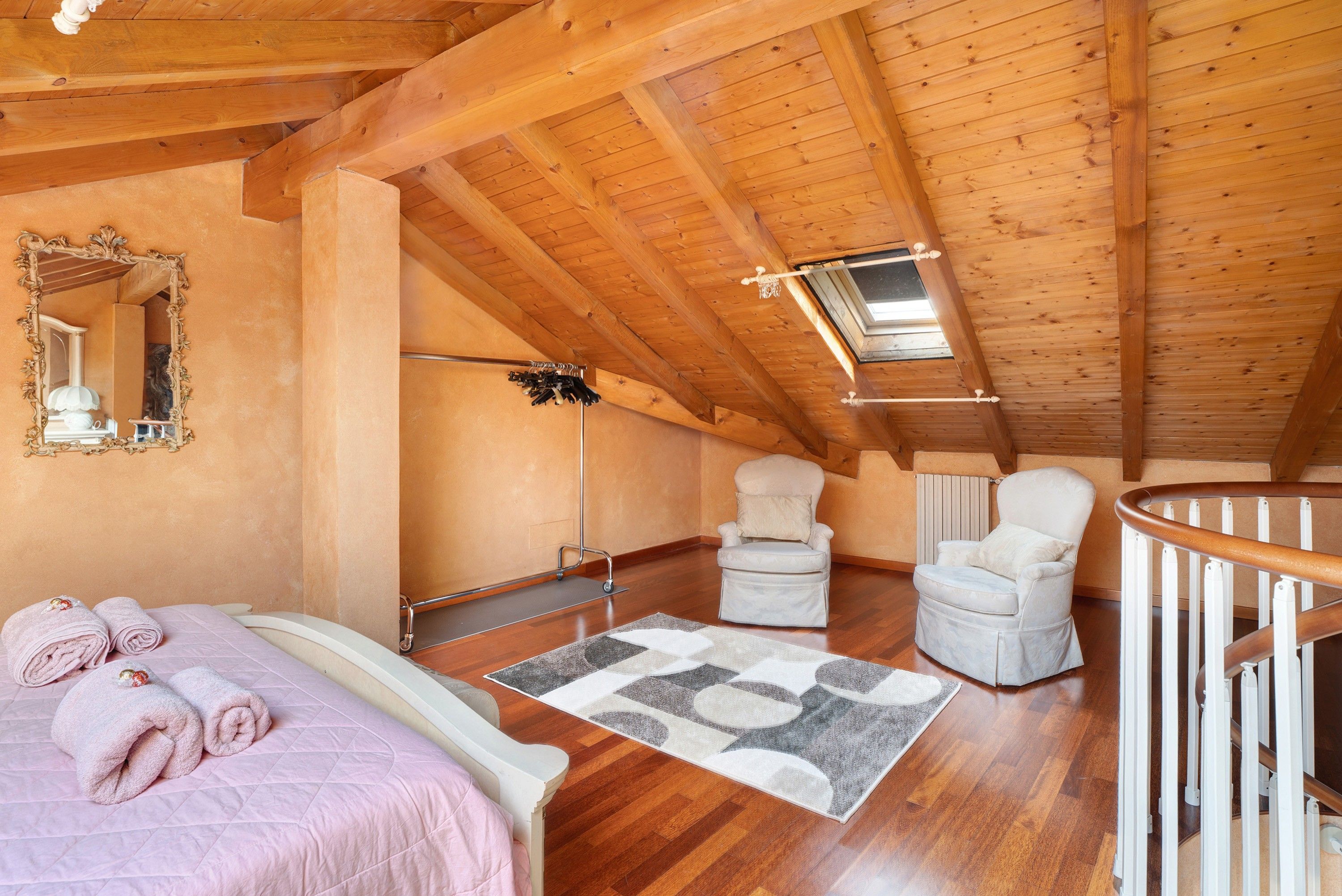 Ein Schlafzimmer mit Holzboden, einem Bett, einem Stuhl, einem Spiegel und einem Fenster.