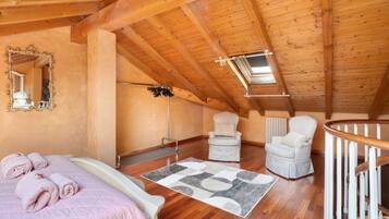 Ein Schlafzimmer mit Holzboden, einem Bett, einem Stuhl, einem Spiegel und einem Fenster.