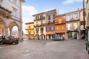 Une rue pavée bordée de bâtiments historiques, une voiture garée et un piéton.