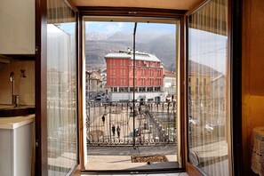 Vista desde una ventana que muestra un edificio, una valla de metal en primer plano y montañas al fondo.