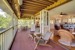A covered porch with wooden flooring, a dining area with chairs and a table, and a kitchen with a counter and chairs.