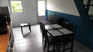 A small, well-lit room with a dining table and chairs, a sofa, and a TV.