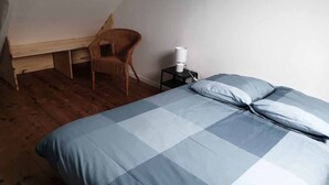 A bedroom with a bed, a chair, a desk, and a nightstand with a lamp.