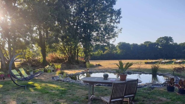 A garden with a wooden table and chairs, surrounded by potted plants and a small pond.