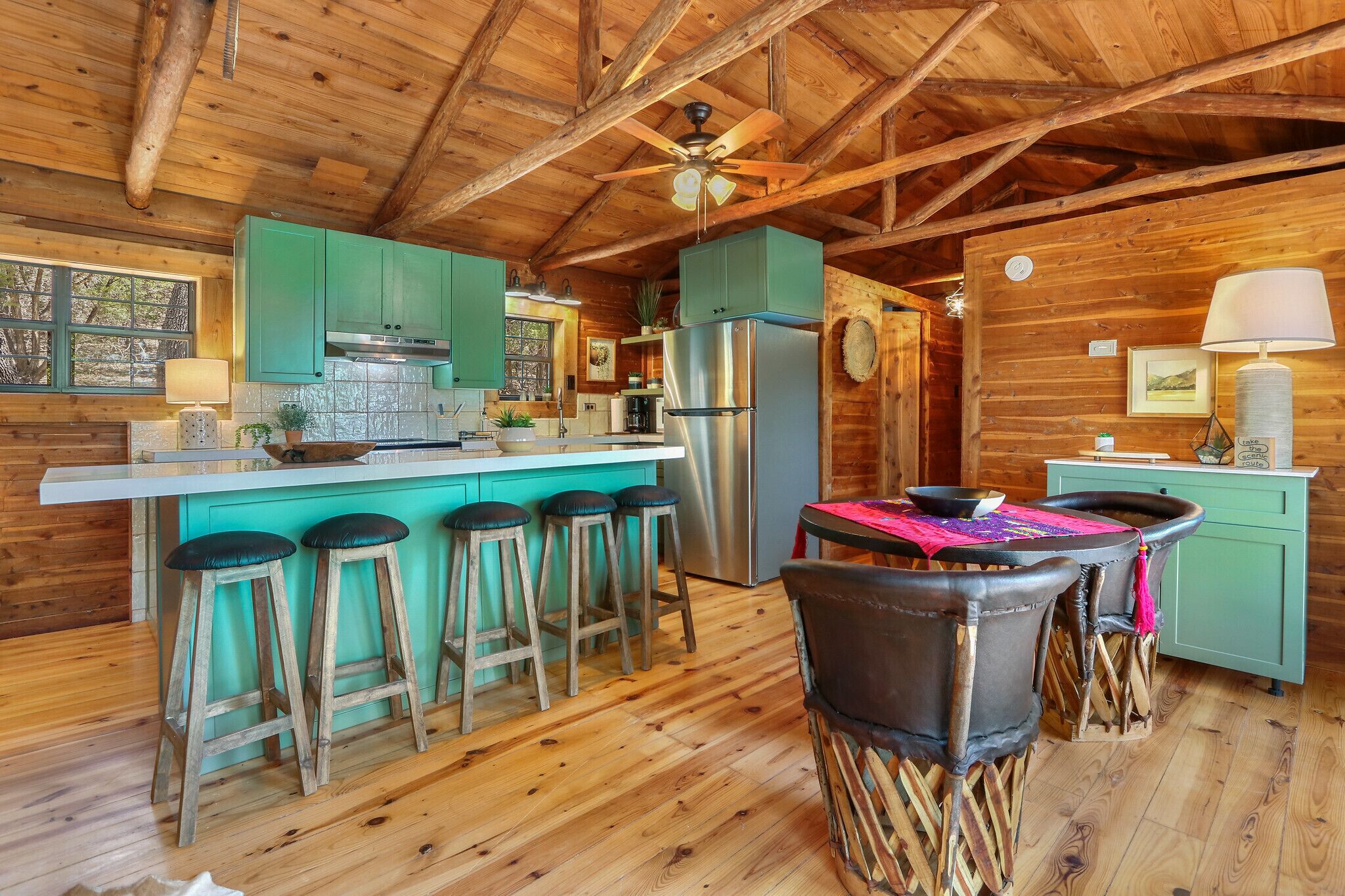 Una cocina rústica con vigas de madera, una isla central con taburetes, un refrigerador y un comedor con sillas.