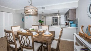 A dining area with a wooden table set for four, surrounded by chairs with cushioned seats. - Seacove in Indian Shores, Beachfront with a pool! (Indian Shores)