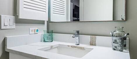Une salle de bain avec un meuble-lavabo blanc, un évier, un miroir et un luminaire placé au-dessus du miroir.