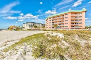 Un hôtel situé en bord de mer, doté de nombreux balcons, avec une plage de sable au premier plan et d’autres bâtiments en arrière-plan.