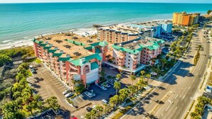 A multi-story hotel with a green roof, adjacent to a beach and ocean, featuring a parking lot and a road. - Seacove in Indian Shores, Beachfront with a pool! (Indian Shores)