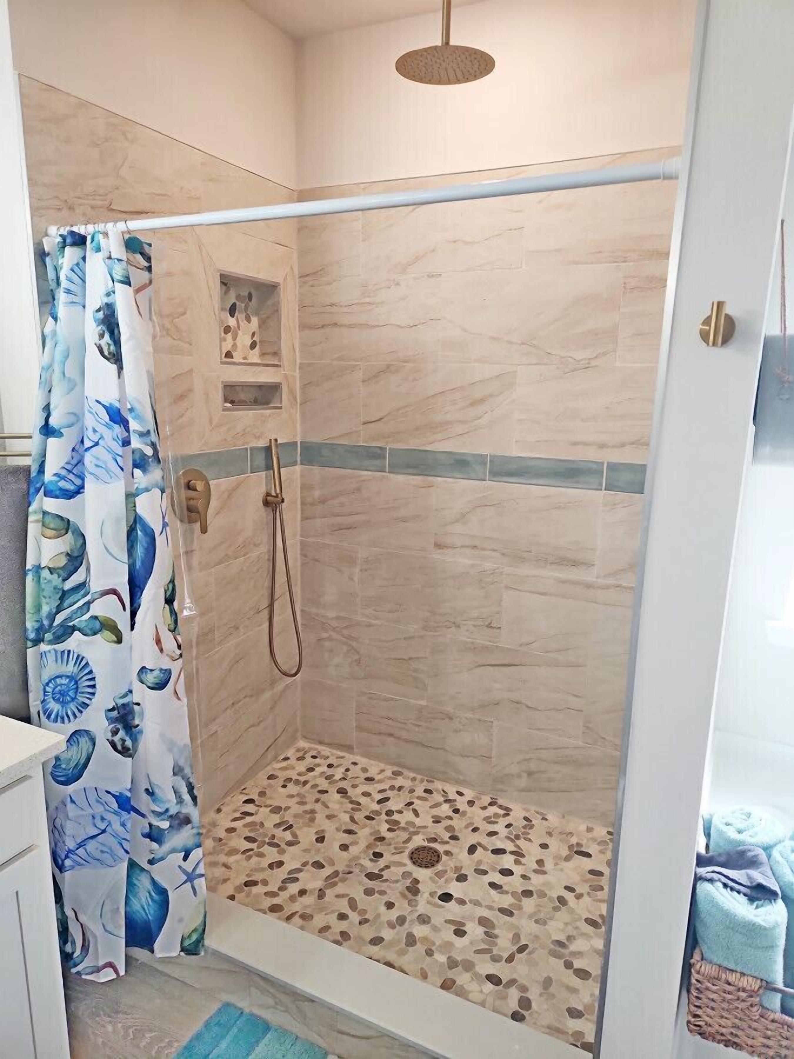 Un espace douche doté d’une porte en verre, d’un pommeau de douche et d’un sol carrelé.
