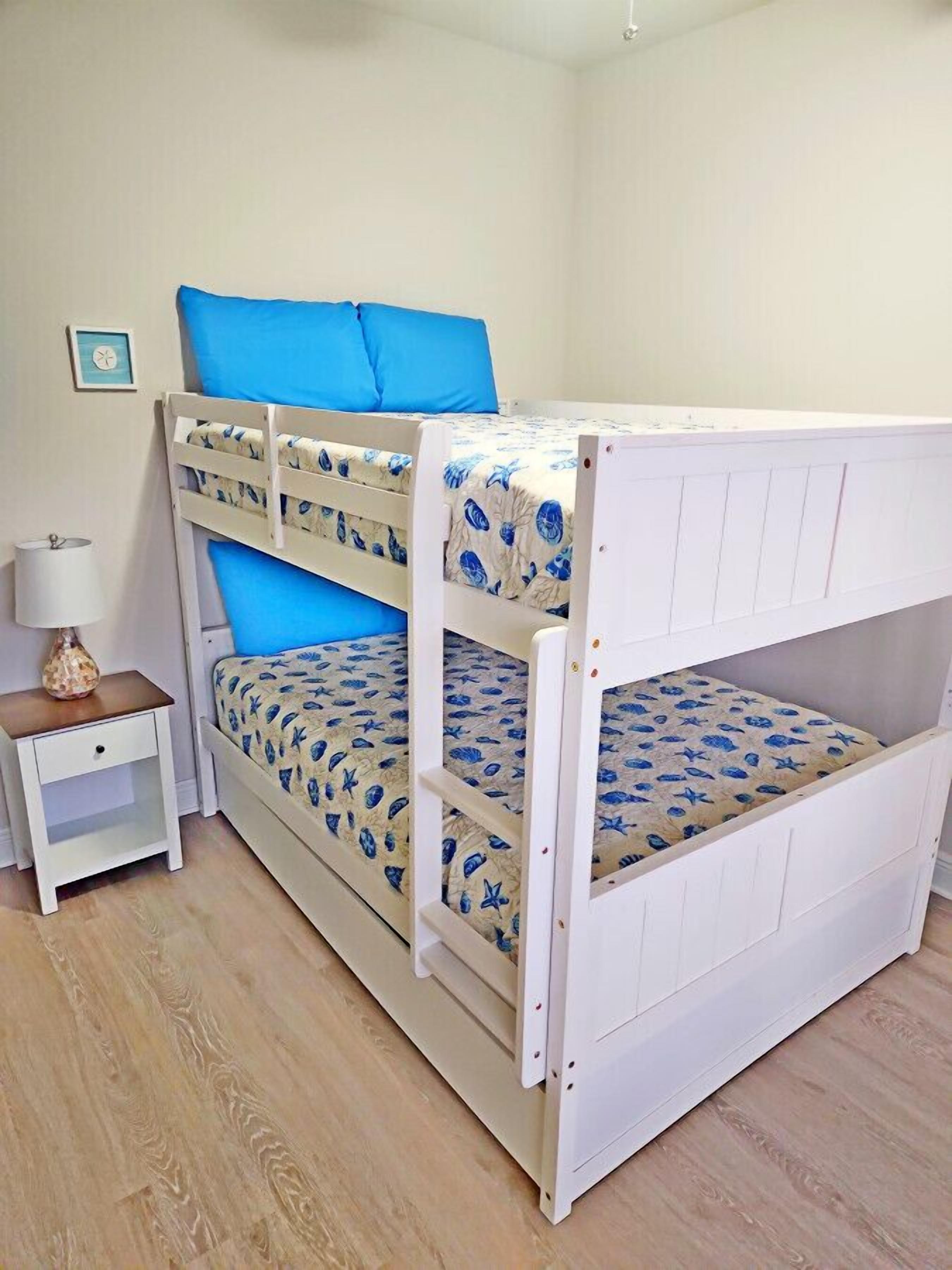A bunk bed with a lower bunk and a top bunk, both with blue bedding. There is a small bedside table with a lamp and a decorative item.