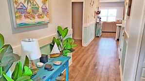 Un couloir avec une table bleue, des plantes et un tableau représentant une maison.