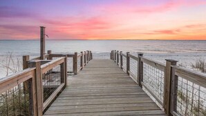 Une promenade en bois menant à une plage, avec un coucher de soleil en arrière-plan.