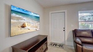 Una sala de estar con un televisor en la pared, una puerta, un sofá de cuero marrón y un mueble consola de madera.
