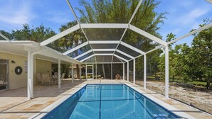 Una piscina cubierta con techo blanco, rodeada por un patio empinado y árboles.