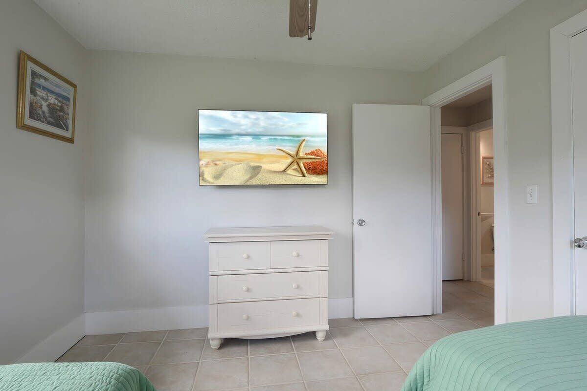 A bedroom with a bed, a dresser, a door, and a wall with a framed picture.