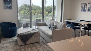 En moderne stue med sofa, skammel og spisebord. Store vinduer giver udsigt til omgivelserne.
